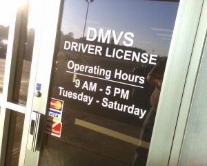 Photo of exterior door of motor vehicle office, showing operating hours, accompanying article on motor voter law.