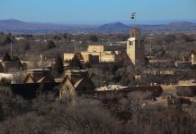 A middle-distant view of Santa Fe with mountains in the far distance, under a hazy blue sky.