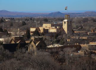 A middle-distant view of Santa Fe with mountains in the far distance, under a hazy blue sky.