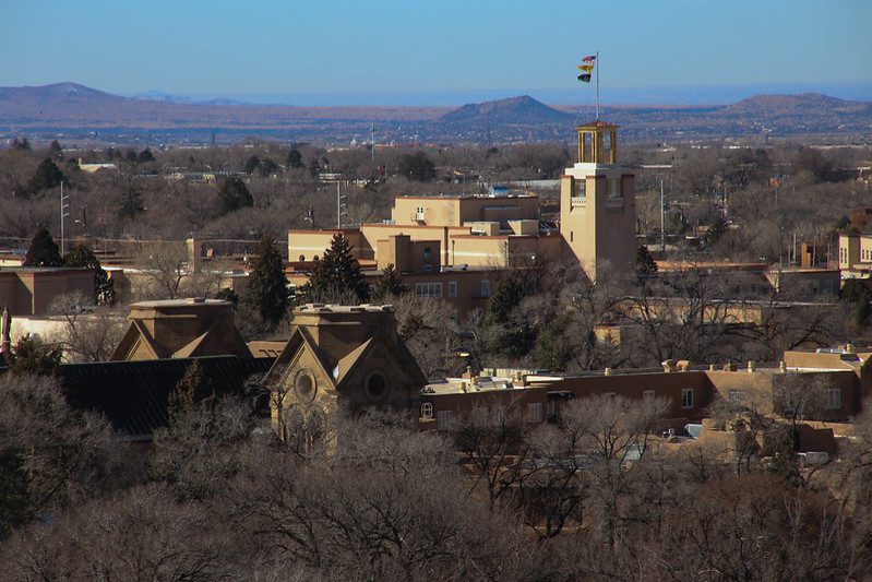 Cityscape of Santa Fe with mountains in the background under a blue sky.