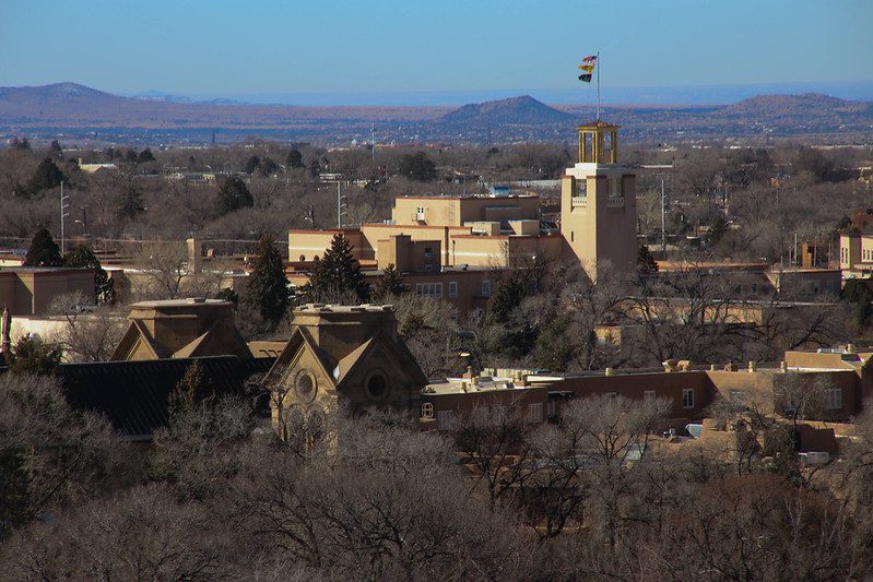 A middle-distant view of Santa Fe with mountains in the far distance, under a hazy blue sky.