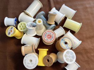Illustrating an article on low-income housing: on a brown fabric background, about two dozen empty spools lie in a disorderly pile. The label on the spool in the center says "American Thread Co."