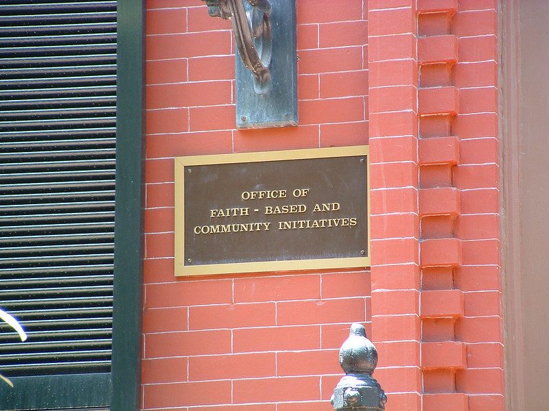 Closeup of plaque on exterior red-brick wall, which reads Office of Faith-Based and Community Initiatives