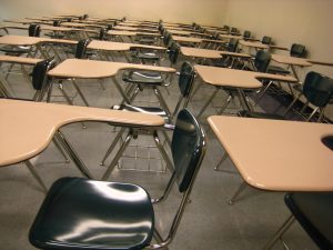 A sepia-toned photo of rows of modern desks with attached chairs in a classroom. 