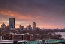 A winter afternoon view of Boston, seen from the south, with an orangey sky behind the city skyline.
