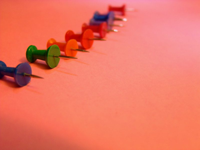 Closeup view of eight pushpins lying on their sides in a gently curved row.