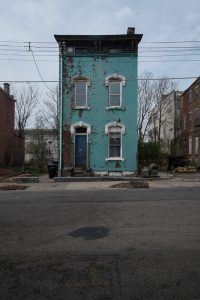 A derelict aqua blue house in Cincinnati's West End neighborhood, taken from across the empty street. There are no people in the photo.