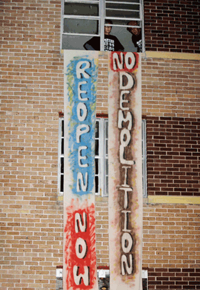 Hand-lettered vertical banners in red and blue spell out "Reopen now" and "No demolition" to illustrate a brief about rebuilding in New Orleans
