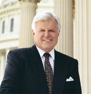 Formal portrait of Sen. Edward Kennedy. Taken outdoors in front of stone columns. He is wearing a suit and tie.