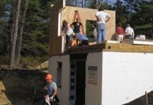 Several workers stand on a partially finished home with white insulation around the foundation.
