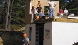 Several workers stand on a partially finished home with white insulation around the foundation.