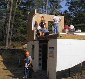 Several workers stand on a partially finished home with white insulation around the foundation.