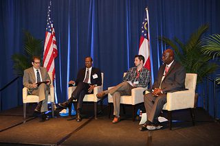 Photo shows a panel of four people in chairs at the National Housing Conference, 2013. From left, they are Chris Estes, Egbert Perry, Samuel Kirkland, and Noel Khalil.