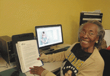 A smiling senior citizen sits at a computer.