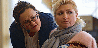 Two women, one on the right stares off camera as the other bends to speak to her.