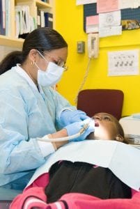 A female dentist cleans a young boy's teeth.