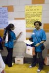 Two students wearing blue shirts stand in front of posters in their school.