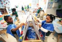 Two young students wear smocks as they paint in school.
