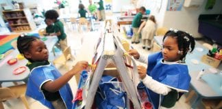 Two young students wear smocks as they paint in school.
