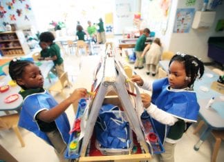 Two young students wear smocks as they paint in school.