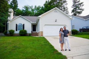 A woman and man stand together smiling in front of their new home in North Carolina. They received a loan not based on credit scores, but on character.
