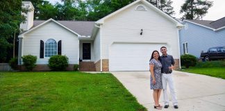 A woman and man stand together smiling in front of their new home in North Carolina. They received a loan not based on credit scores, but on character.