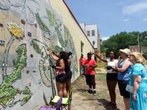 Various people work to put tiles on a wall to complete a mural.