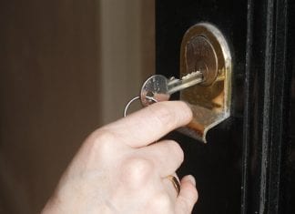A white hand puts a silver colored key into a door lock.
