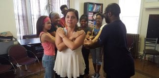 A member of a New Jersey based advocacy group crosses her hands over her chest and her fellow group members line up behind her with their arms extended. This is a trust fall.