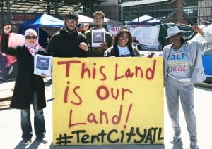 Residents of four historically African-American neighborhoods hold up a sign that reads "This Land is Our Land! #TentCityATL"