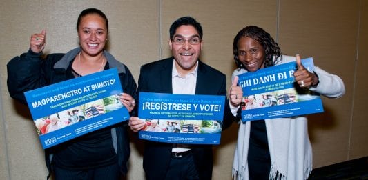 Three members of the Non-Profit Housing Association of Northern California give a thumbs up as they hold "Register and Vote" signs in different languages.
