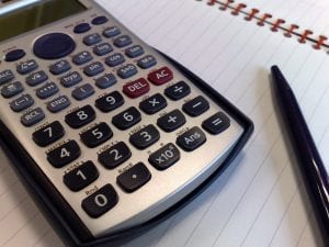 A calculator and black pen lie upon a double ruled notebook.