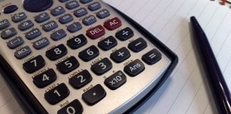 A calculator and black pen lie upon a double ruled notebook.