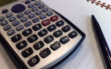 A calculator and black pen lie upon a double ruled notebook.