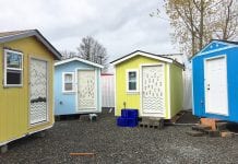 Front of four small houses, colored tan, light blue, yellow, and deep blue with a door and one window.