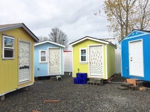 Front of four small houses, colored tan, light blue, yellow, and deep blue with a door and one window.