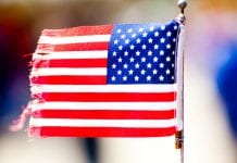 Small American flag with fringed edges attached to a wire stick.
