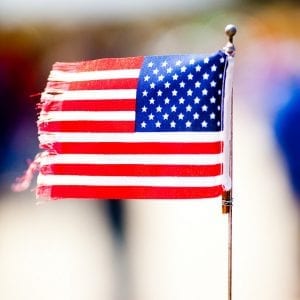 Small American flag with fringed edges attached to a wire stick.