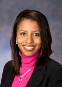 Angela Mingo poses for a headshot wearing a black blazer and a pink turtle neck shirt.