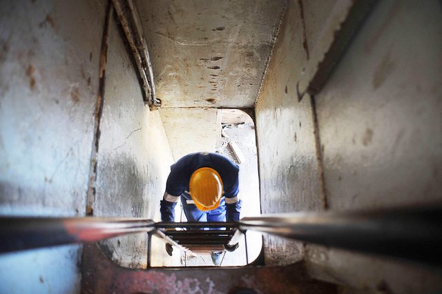 View of a worker's hard hat as they climb on a ladder in a tunnel.