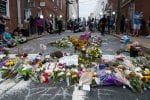 A street is covered with flowers and photos of Heather Heyer, as people look on the background