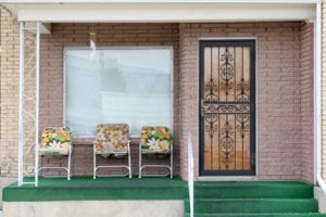 Front porch with three floral chairs in front of a window and a green floor.