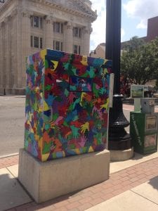 Public art in Pittsfield, Massachusetts: A utility box on a sidewalk is covered with interlocking hands in all the colors of the rainbow.