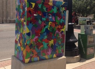 Public art in Pittsfield, Massachusetts: A utility box on a sidewalk is covered with interlocking hands in all the colors of the rainbow.