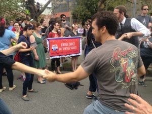 A white man is dancing in the foreground with someone who is out of the frame, in front of a red banner reading "Vinage Dance, Not Vintage Values" and "Swing Dancers for Justice and Equality"