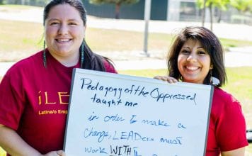 Two woman hold a sign that reads, "Pedagogy of the Oppressed Taught me ..."