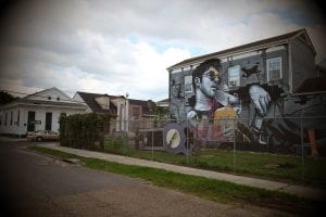 A sprawling white “hipster” is memorialized against a backdrop of romanticized visions of blight in a mural that dominates an intersection in the historically Black 7th Ward in New Orleans.