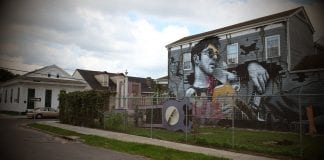 A sprawling white “hipster” is memorialized against a backdrop of romanticized visions of blight in a mural that dominates an intersection in the historically Black 7th Ward in New Orleans.