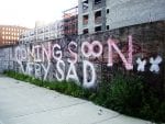 "Coming Soon, Very Sad" painted on border wall outside of new development.