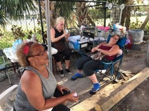 Three women sitting on chairs on a sidewalk.